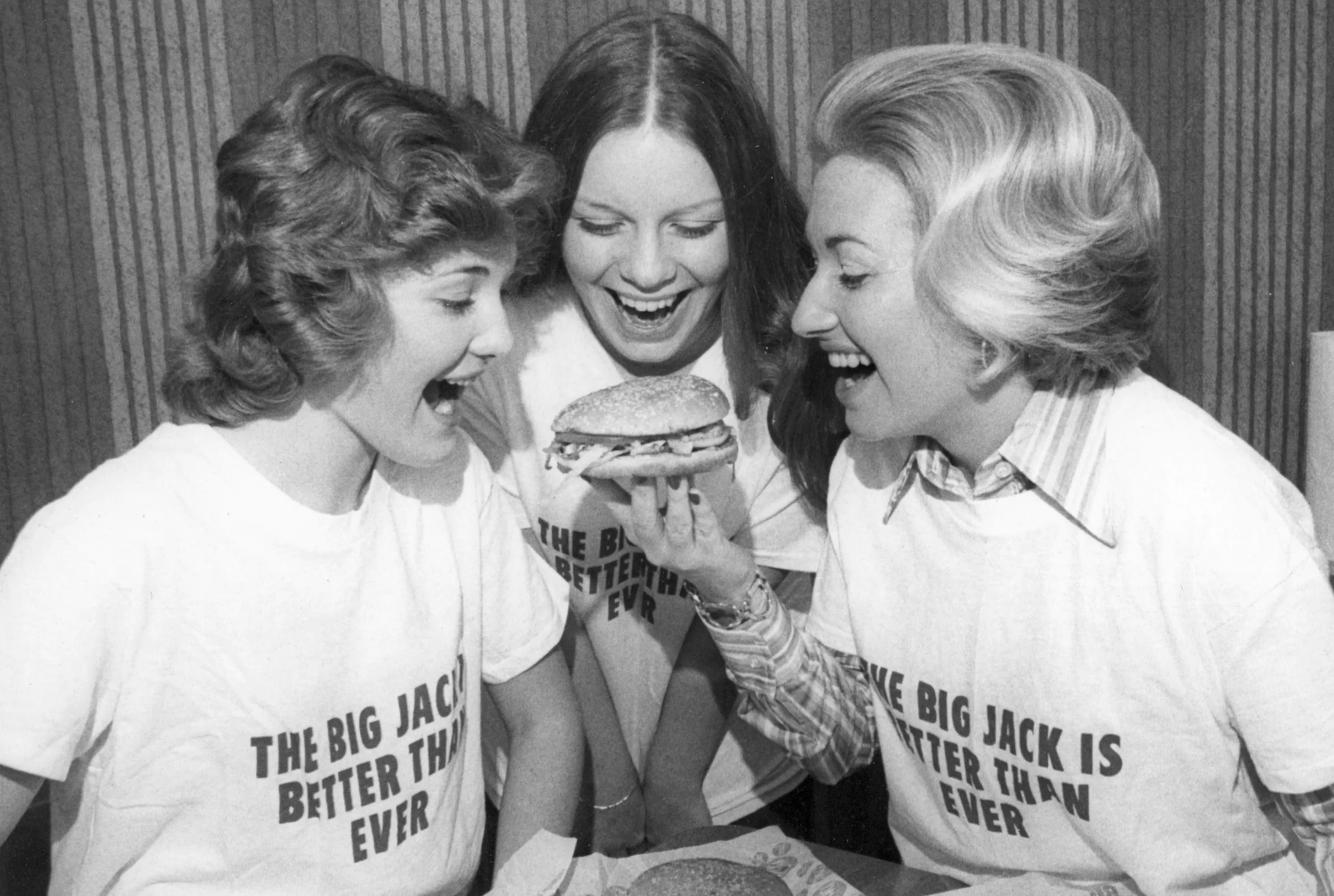 Vintage photo of three women and one of them is holding a Jack's cheeseburger.
